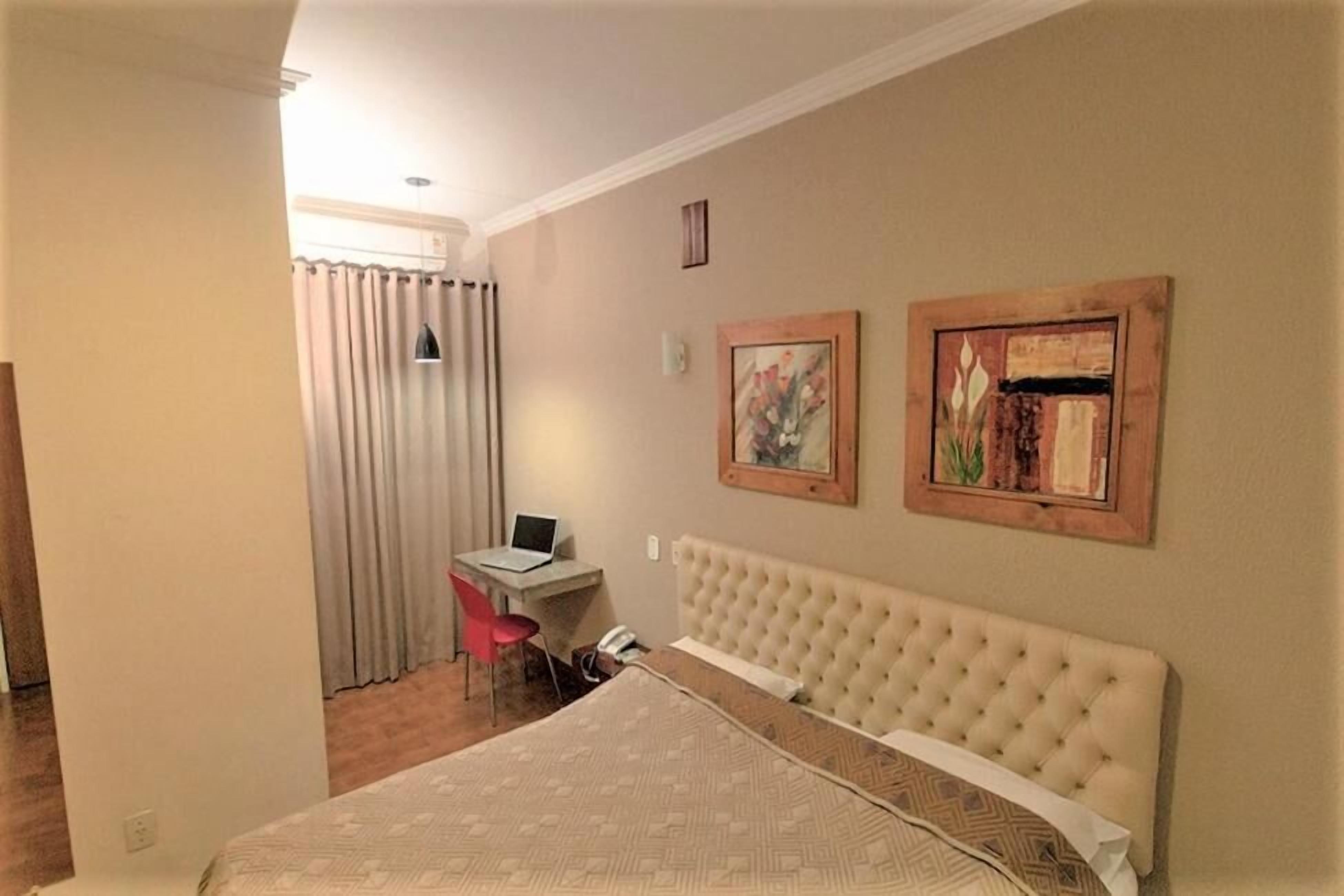 Habitación de hotel con cama, un escritorio con una computadora portátil, una silla y dos cuadros en la pared.
