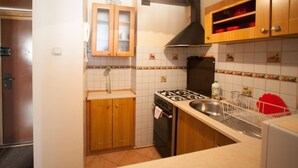 A compact kitchen with wooden cabinets, a gas stove, a sink, and a hanging light fixture. - Apartamenty Varsovie Sliska (Warsaw)
