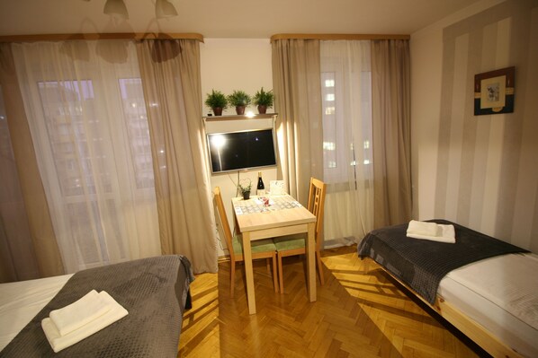 Hotellihuone, jossa on kaksi erillistä sänkyä, puinen pöytä tuoleineen, televisio ja ikkuna, jossa on verhot.