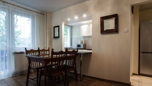 A dining area with a wooden table and chairs, a kitchen with a refrigerator and microwave, and a window with curtains. - Apartamenty Varsovie Superb Panska 5 (Warsaw)