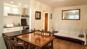 A modern kitchen with white cabinets, a wooden dining table, and a sofa in the living area. - Apartamenty Varsovie Superb Panska 5 (Warsaw)