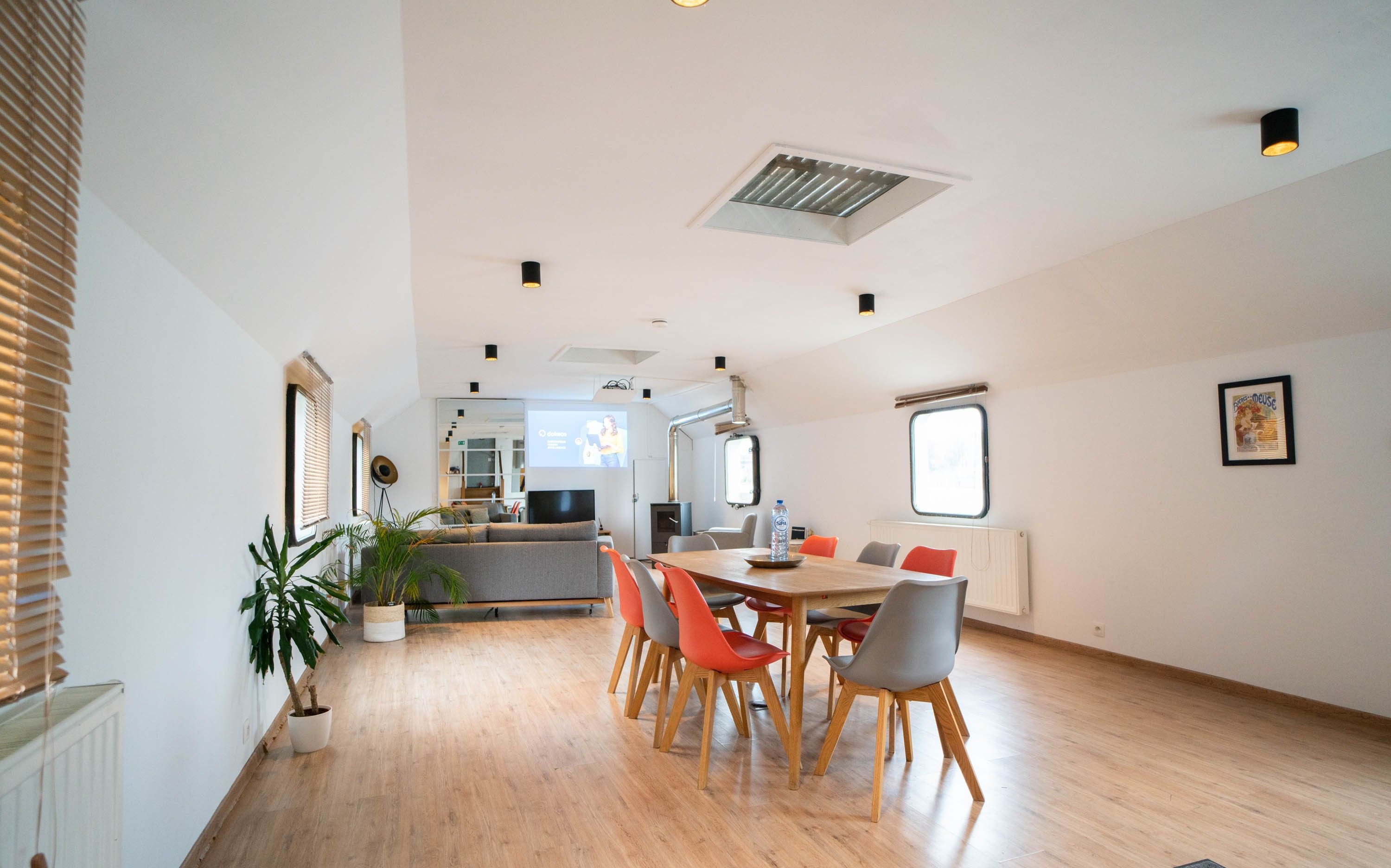 Un grand salon doté d’un plancher en bois, d’une table à manger avec des chaises et d’un canapé. On y trouve également des plantes en pot et un radiateur fixé au mur.