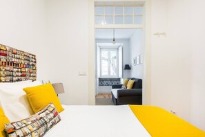 Un dormitorio con una cama, una mesita de noche, una lámpara, una ventana y vistas a un salón.