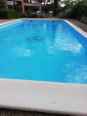 Ein rechteckiger Swimmingpool mit weißem Rand und blauer Innenseite. Am Ende des Pools stehen zwei weiße Stühle.