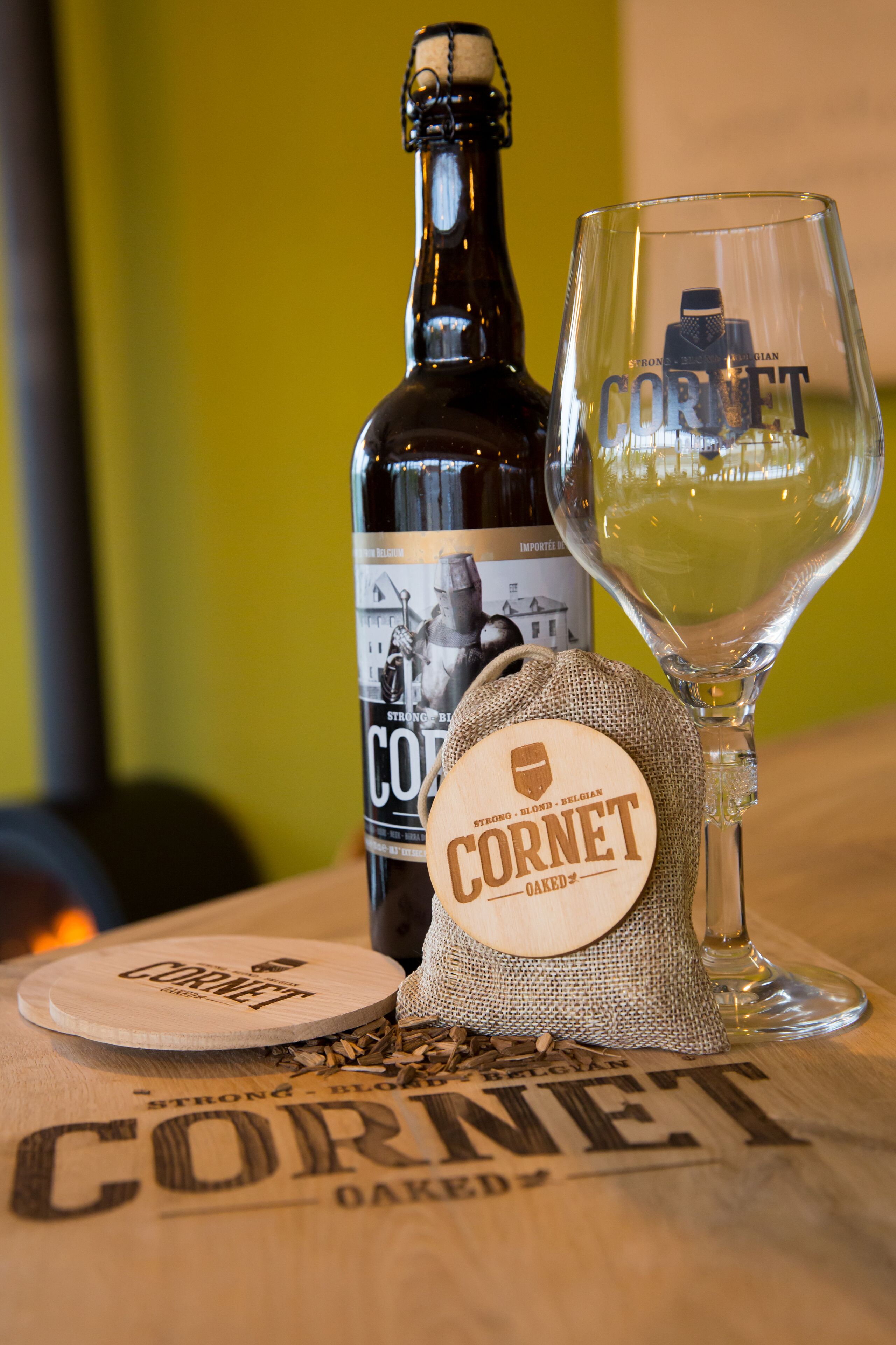 Een fles Coronet bier, een glas bier en bierviltjes met het Coronet logo op een houten tafel.