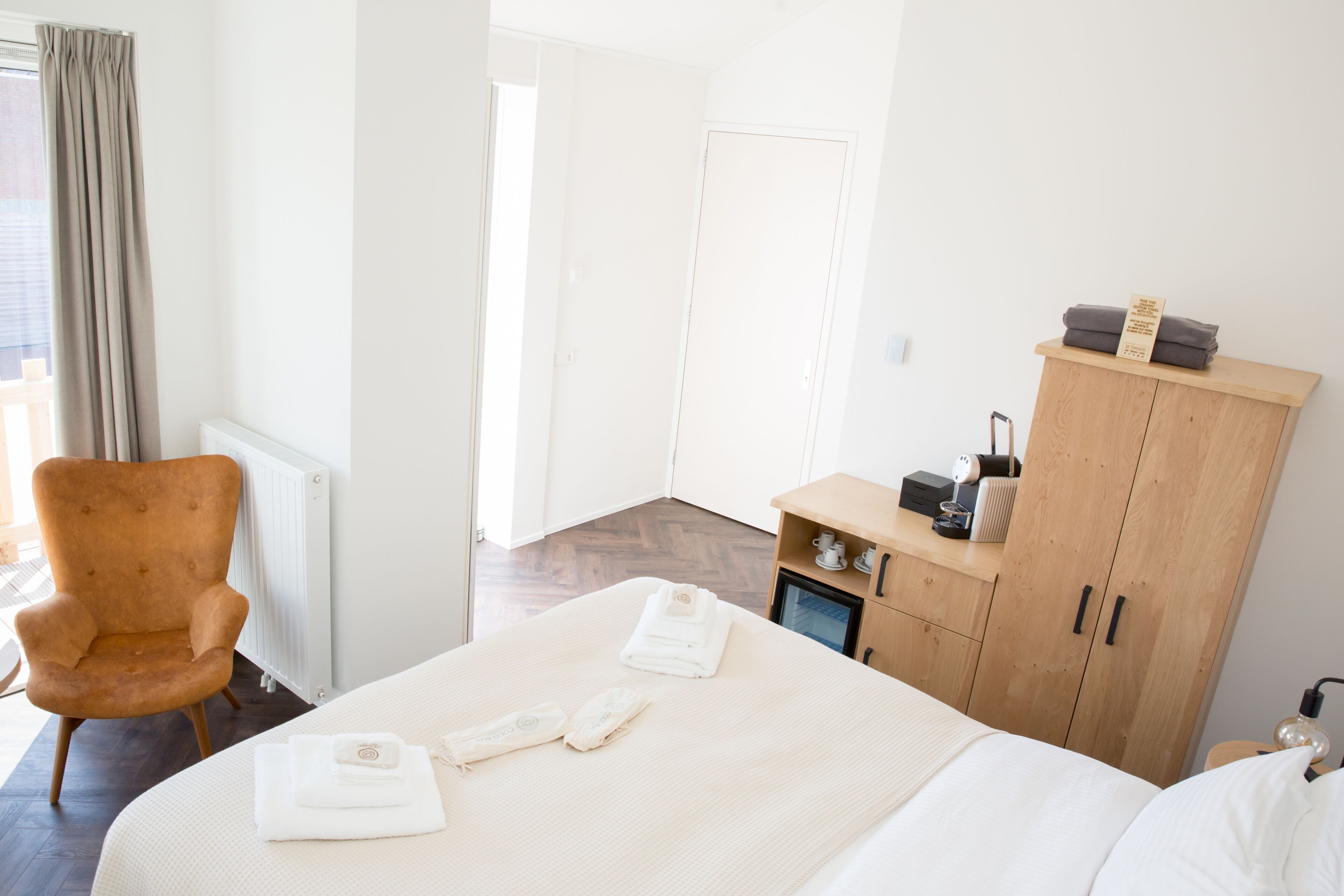 A hotel room with a bed, a wooden wardrobe, a chair, and a radiator.
