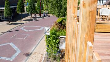 Een verharde weg met fietspad, een houten hek en een aangelegde tuin met kleine struiken en een bloembed.