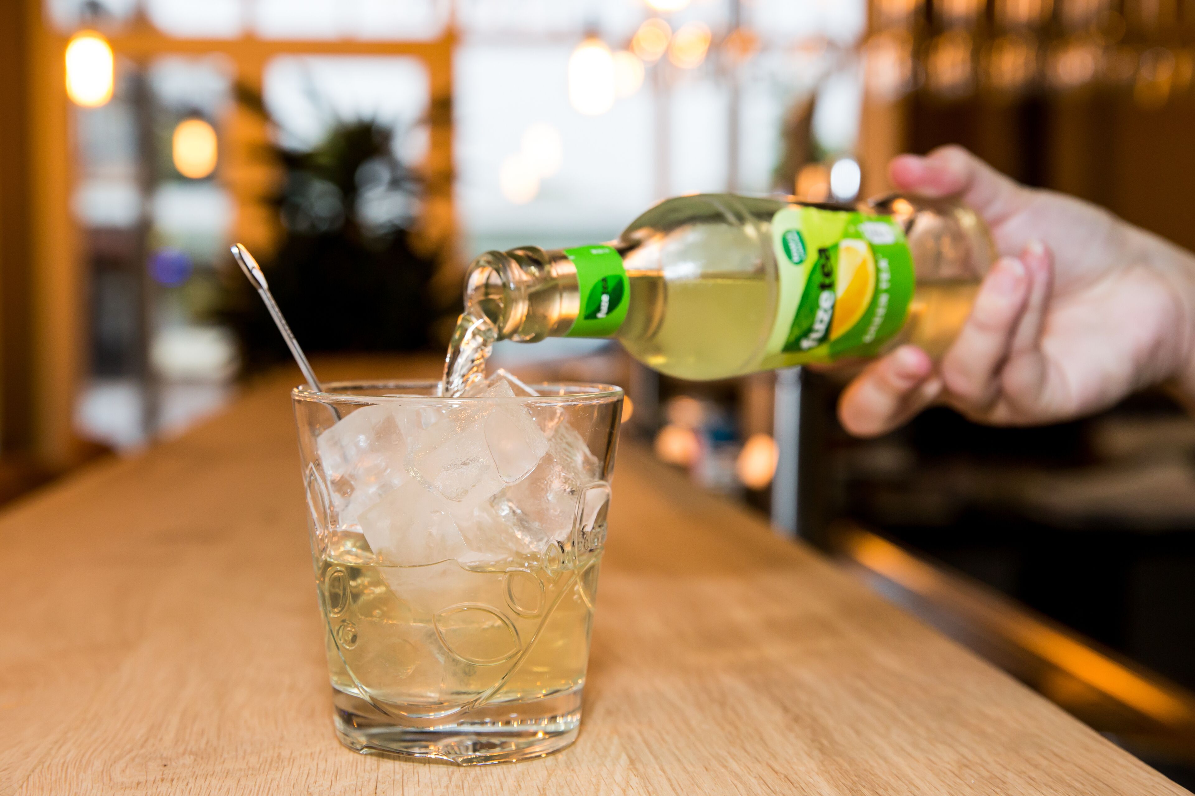 A hand pouring a drink into a glass with ice cubes.