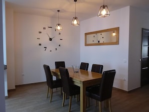A dining area with a wooden table and black chairs, a wall clock, pendant lights, and a mirror.