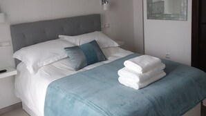 A neatly made bed with white and teal bedding, a gray headboard, and a teal throw blanket.