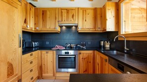 A modern kitchen with wooden cabinets, a Bosch oven, and a black countertop. - Chalet Teremok - Jacuzzi & Sauna - Great for families (Riddes)