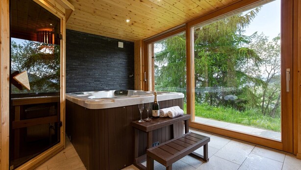 A modern bathroom with a wooden ceiling, a black wall, and a large window offering a view of trees. - Chalet Teremok - Jacuzzi & Sauna - Great for families (Riddes)