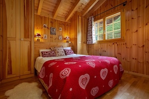 Un dormitorio de cabaña de madera con una cama, paredes de madera, un ventanal y lámparas fijadas a la pared.