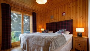 A cozy wooden room with a large bed, two bedside tables with lamps, and a window with curtains. - Chalet Teremok - Jacuzzi & Sauna - Great for families (Riddes)