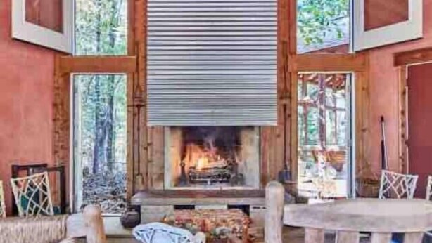 A rustic cabin interior with a central fireplace, wooden beams, and large windows. - Wooded LODGE, Sleeps 9, Pet Friendly, Accessible (Ben Wheeler)