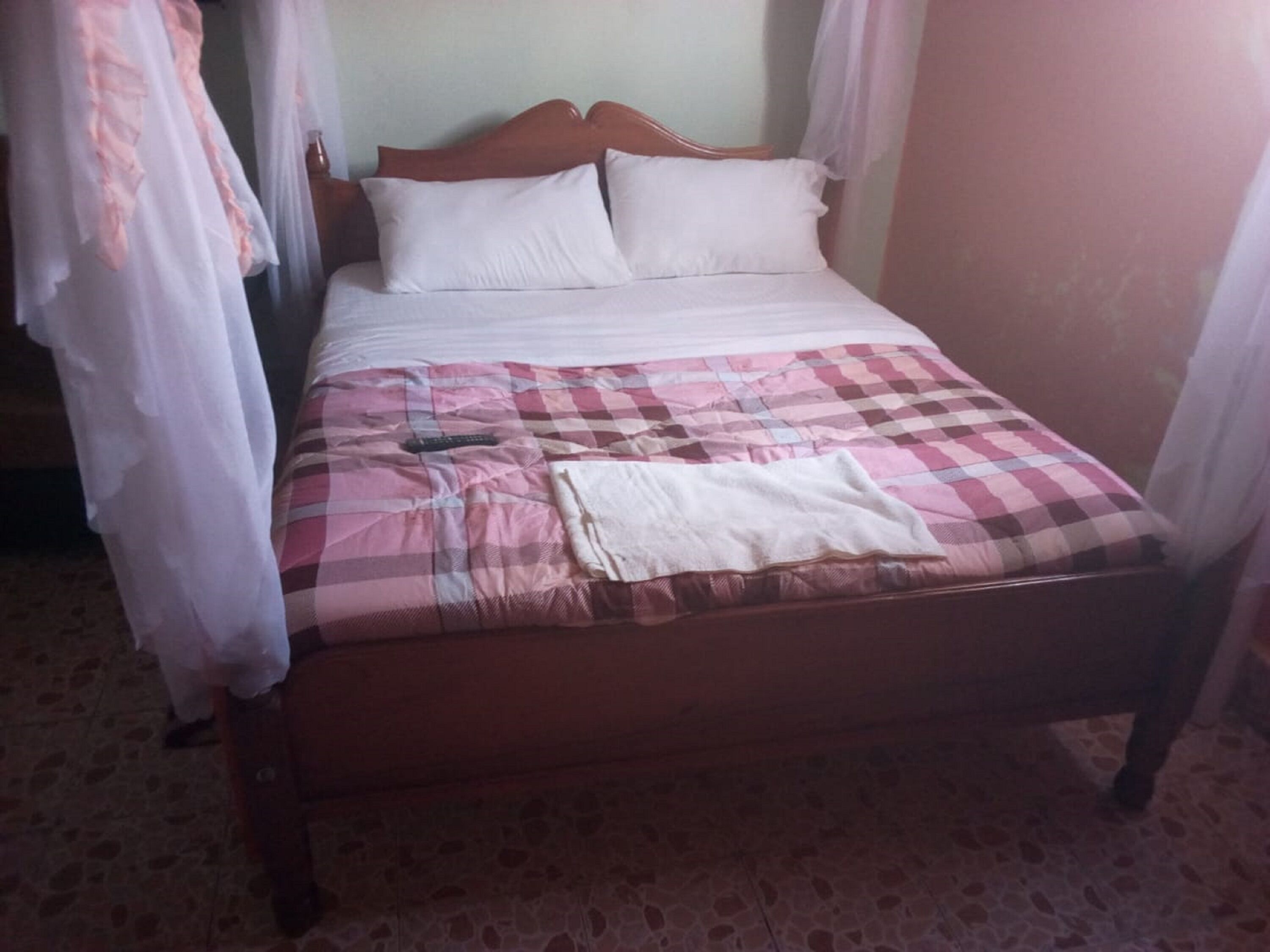 Una cama con una colcha a cuadros, dos almohadas, un control remoto y una toalla doblada.