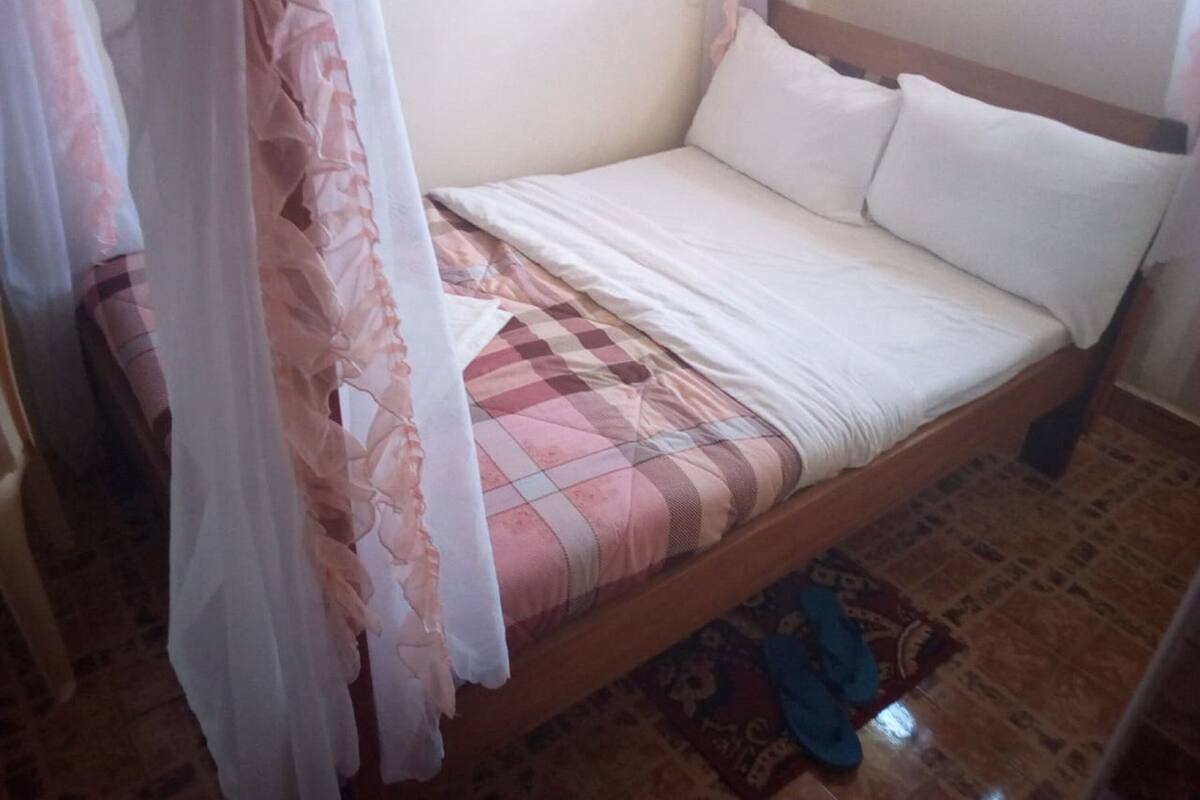 Una cama individual con un edredón a cuadros, almohadas blancas y un dosel ligero.