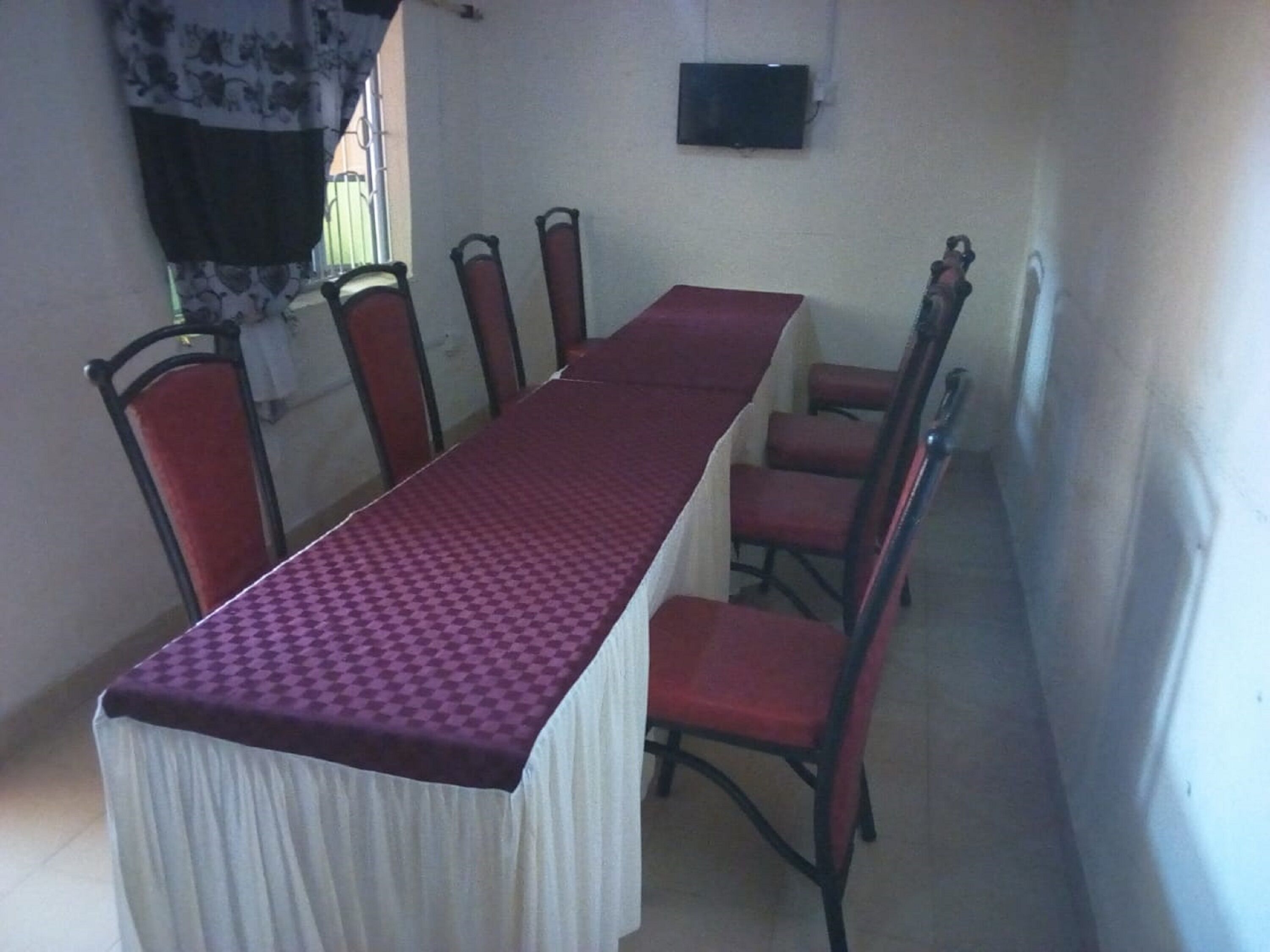A dining area with a long table, red chairs, and a television on the wall.