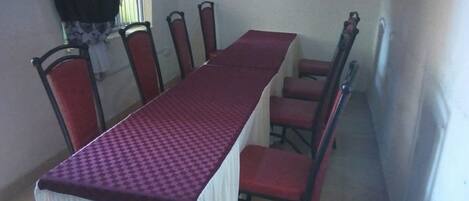A dining area with a long table, red chairs, and a television on the wall.