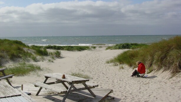 Una playa con una mesa de picnic de madera y una persona sentada sobre la arena.