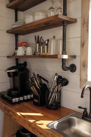 Une cuisine avec des étagères en bois, une machine à café, des ustensiles et un évier.