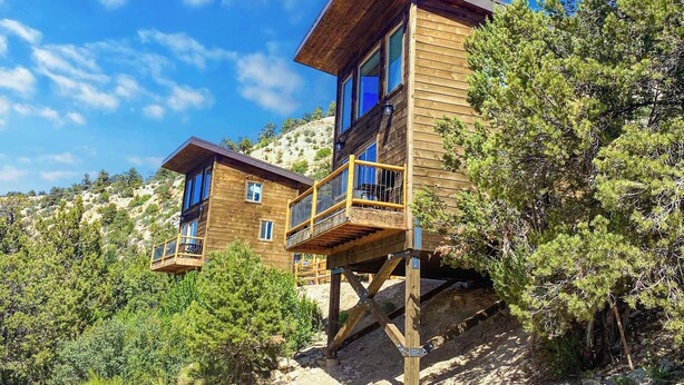 A wooden cabin with a balcony, situated on a hillside with trees.