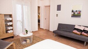 A modern hotel room with a bed, a grey sofa, a wooden wardrobe, a round side table, and a door leading to a bathroom. - Cozy Studio Athens Downtown - Sleeps 3 (Athens)