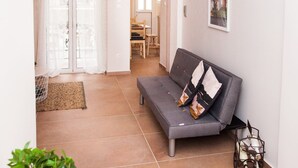 A modern living room with a grey sofa, a small table, and a potted plant. - Cozy Studio Athens Downtown - Sleeps 3 (Athens)