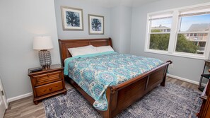 A bedroom with a wooden bed, a nightstand with a lamp, and two framed pictures on the wall. - Oceanside, Private Pool, Hot Tub, 410 ft to Beach Access! CP8, Moore Fun, Less Work (Corolla)