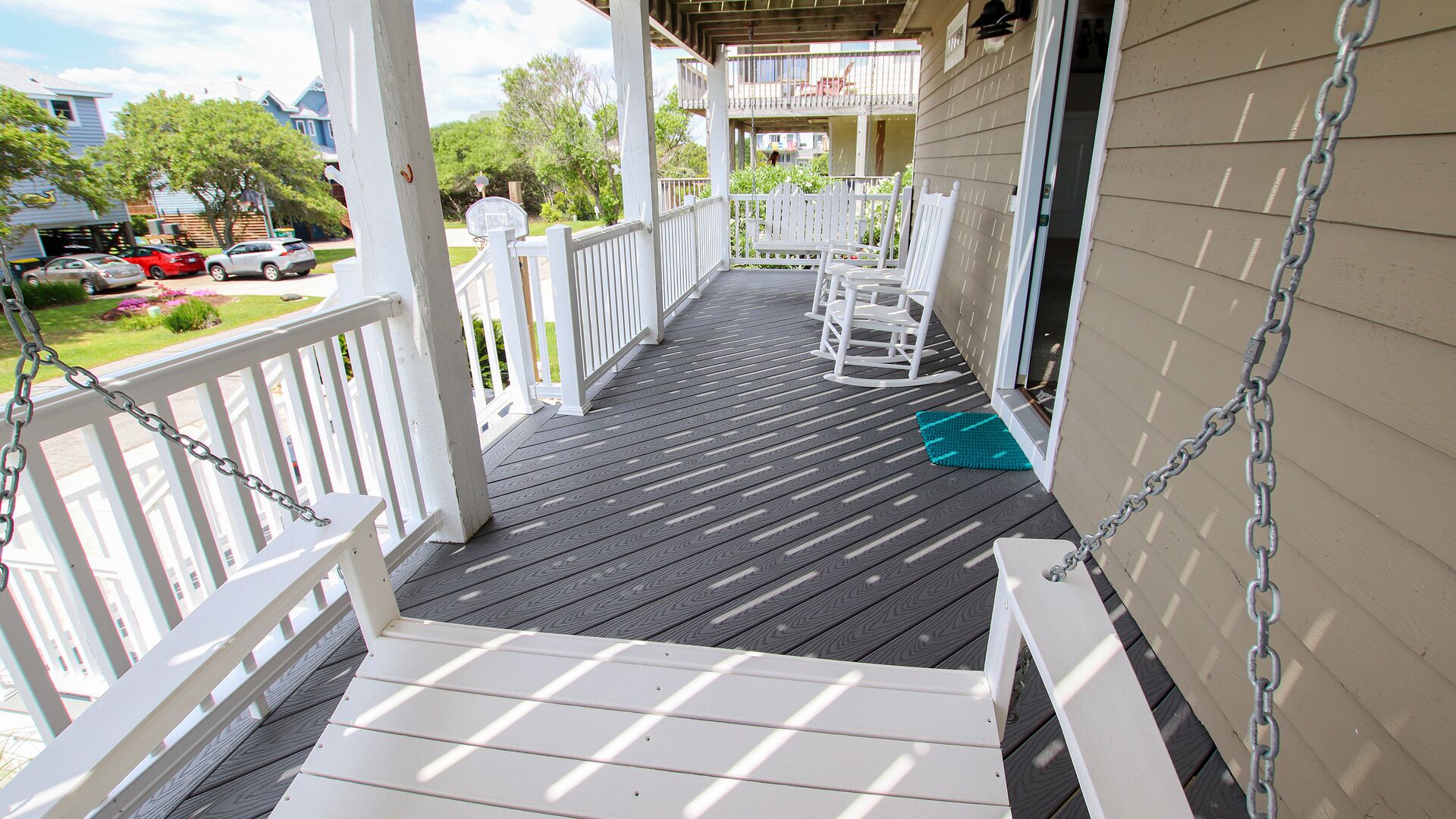 A wooden deck with white railings, a blue mat, and a white chair.