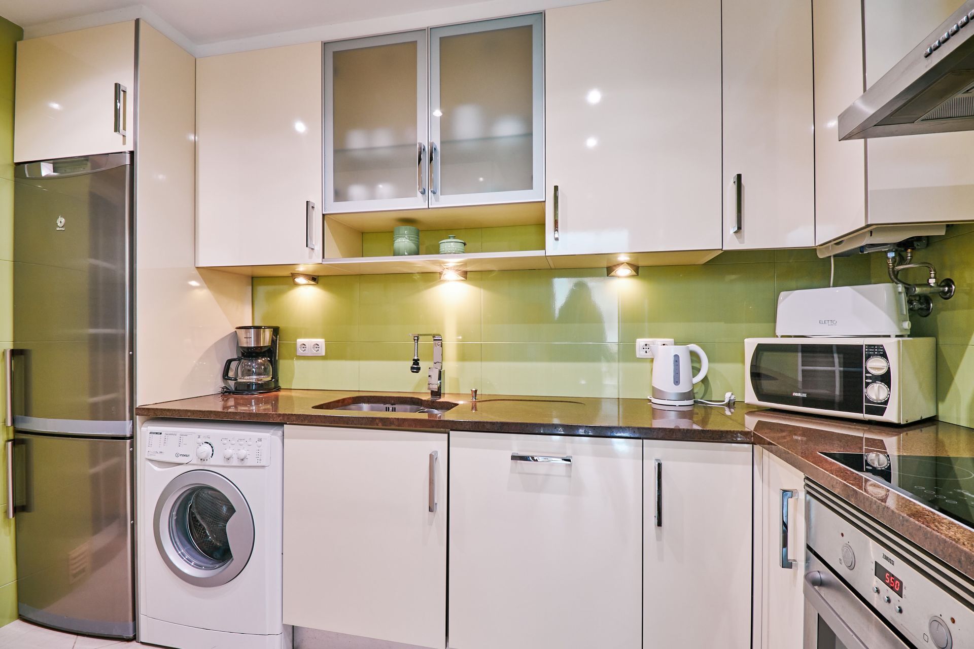 A compact kitchen with a refrigerator, washing machine, microwave, and a coffee maker.