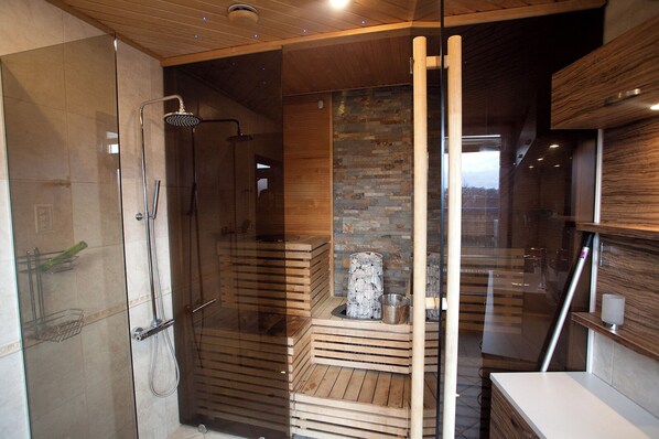 A modern bathroom with a glass shower enclosure, wooden flooring, and a stone wall.