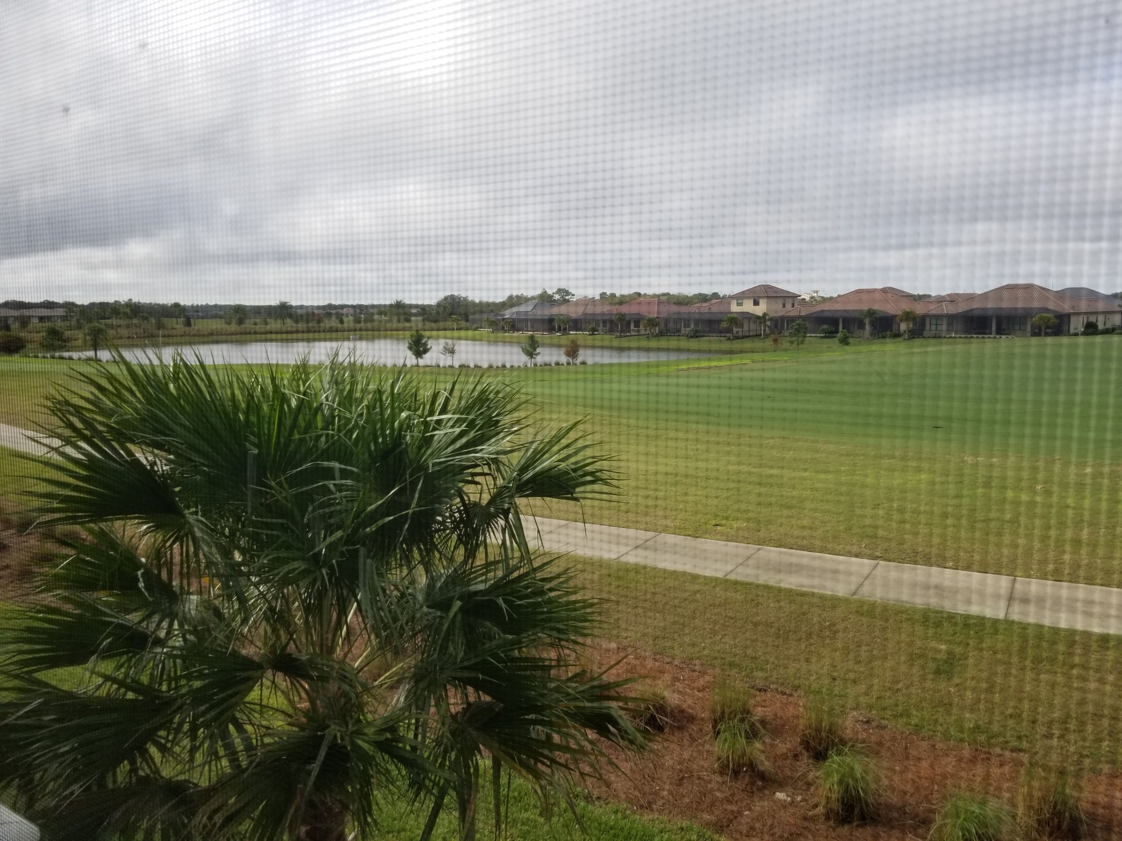 A view of a grassy area with a body of water and houses in the background.