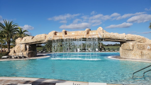 Une piscine agrémentée d’une arche en pierre et de jeux d’eau, de chaises longues et d’un panneau indiquant qu’il est interdit de grimper.