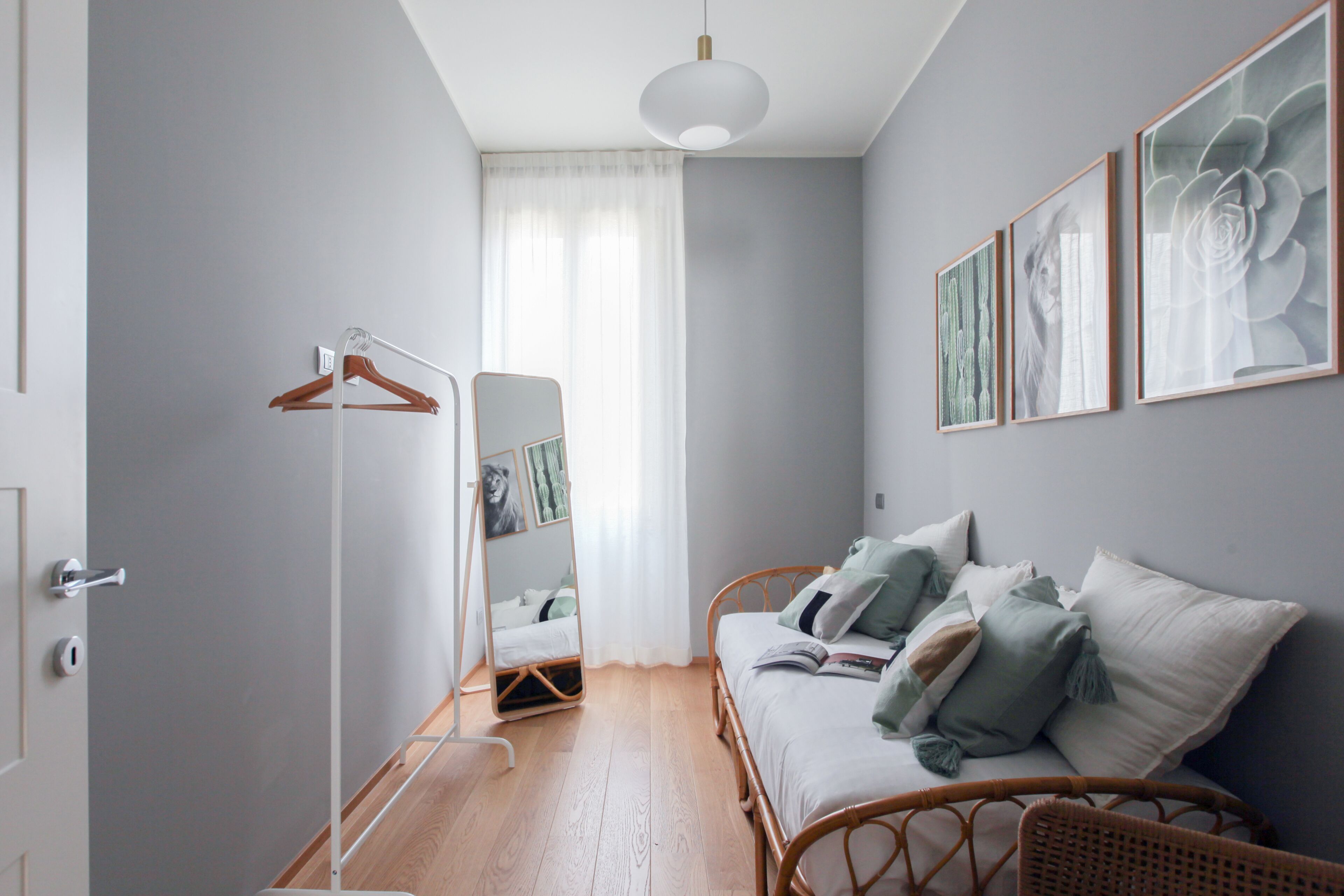 Un dormitorio moderno con suelo de madera, una cama de mimbre, una mesita de noche, un espejo y cuadros en la pared.