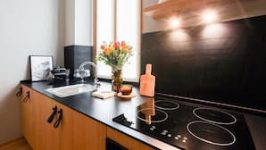 A modern kitchen with a black induction cooktop, wooden cabinets, a stainless steel sink, and a vase with flowers on the counter. - Cà Bèla - Vitruvio (Milan)