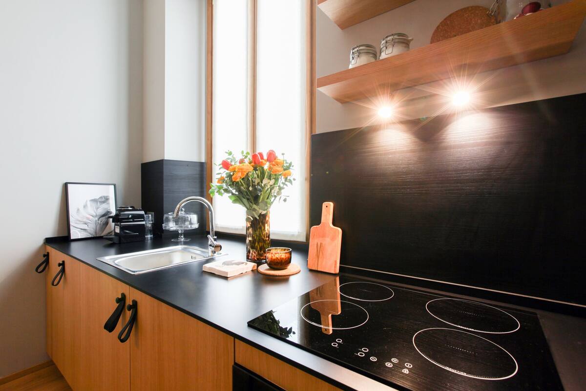 Eine moderne Küche mit einem schwarzen Induktionskochfeld, Holzschränken, einer Edelstahl-Spüle und einer Vase mit Blumen auf der Arbeitsfläche.