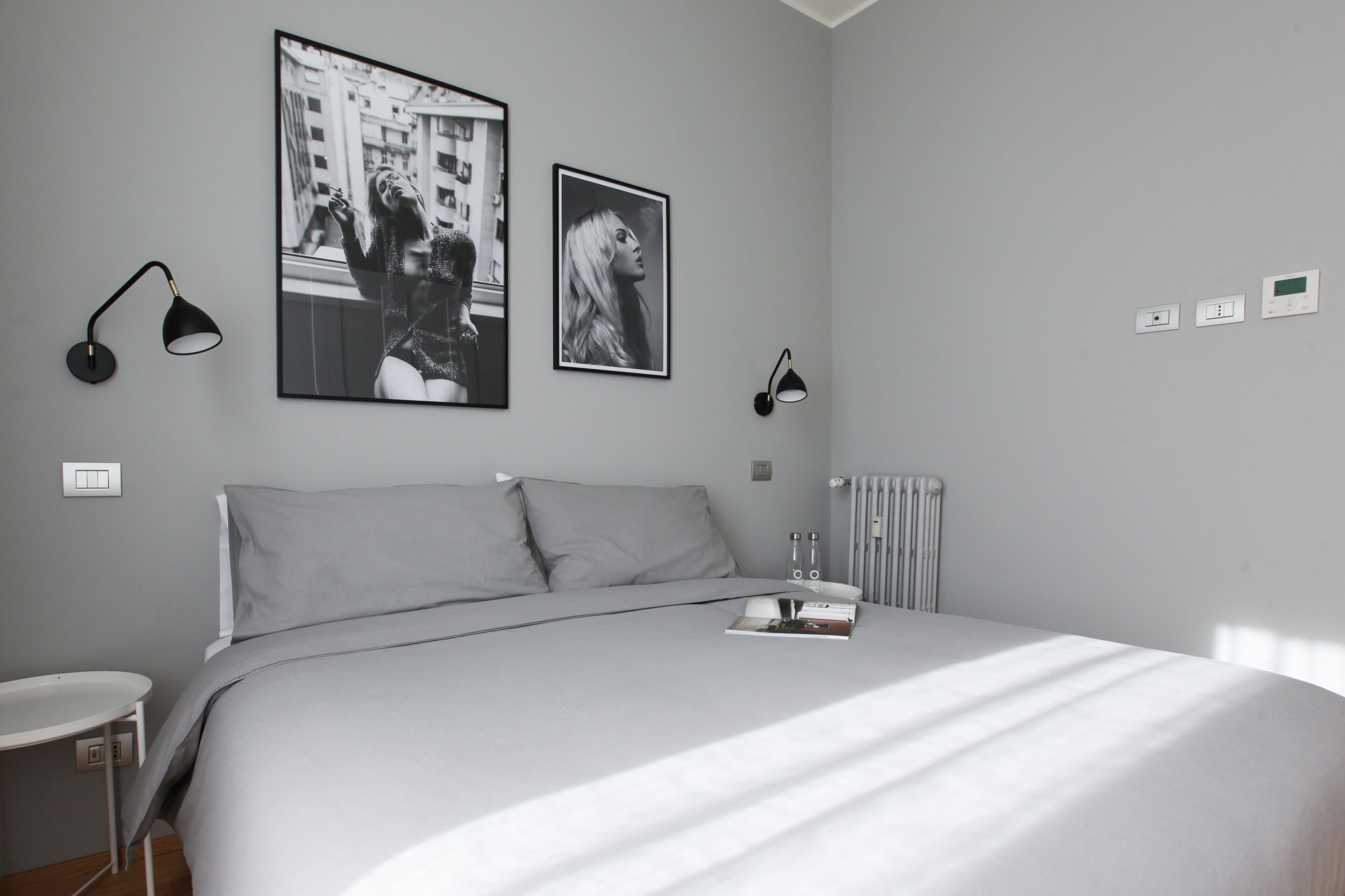 A modern bedroom with a large bed, two wall-mounted lamps, a radiator, and two framed pictures.