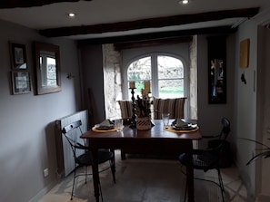 A dining area with a wooden table, two chairs, a vase with flowers, and a window with a view of greenery. - Les Charmes du Lac A Cozy Studio Apartment in the Heart of Esclauzels   (Esclauzels)