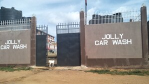 Una entrada con portón a un establecimiento de lavado de autos llamado 'Jolly Car Wash', con un sendero de tierra que conduce a la entrada.