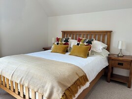 Una cama bien tendida con un edredón estampado, dos almohadas, una mesita de noche con una lámpara y un mueble auxiliar con un cajón.