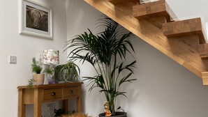 Eine Holztreppe mit Glastrennstäben, ein kleiner Holztisch mit Pflanzen, ein Blumentopf und ein flauschiges braunes Objekt auf dem Boden.