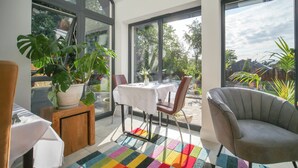 Ein modernes Zimmer mit großen Fenstern, einem Esstisch mit Stühlen, einem grauen Sessel und einem farbenfrohen Teppich.