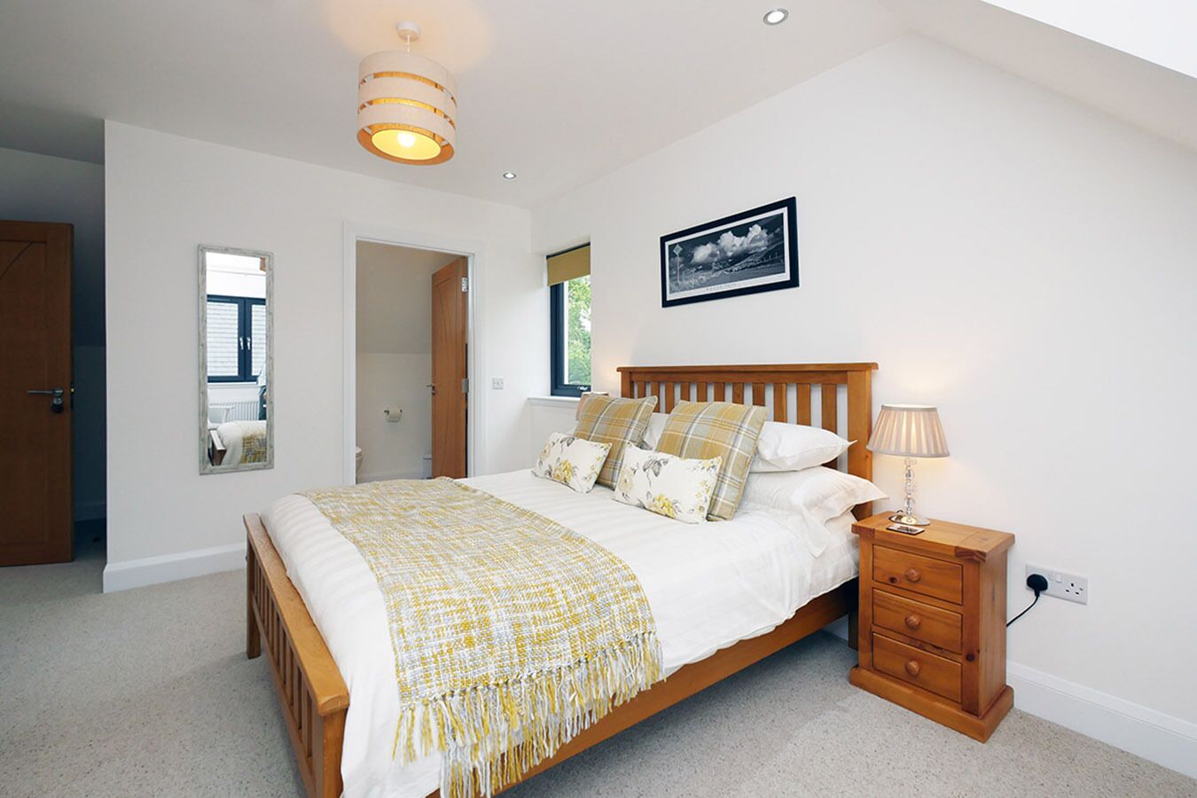 A bedroom with a wooden bed, a bedside table, a nightstand, a mirror, and a ceiling light fixture.