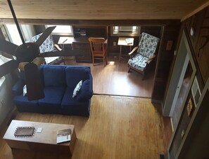A cozy cabin interior with a blue sofa, wooden dining table, and two patterned chairs.