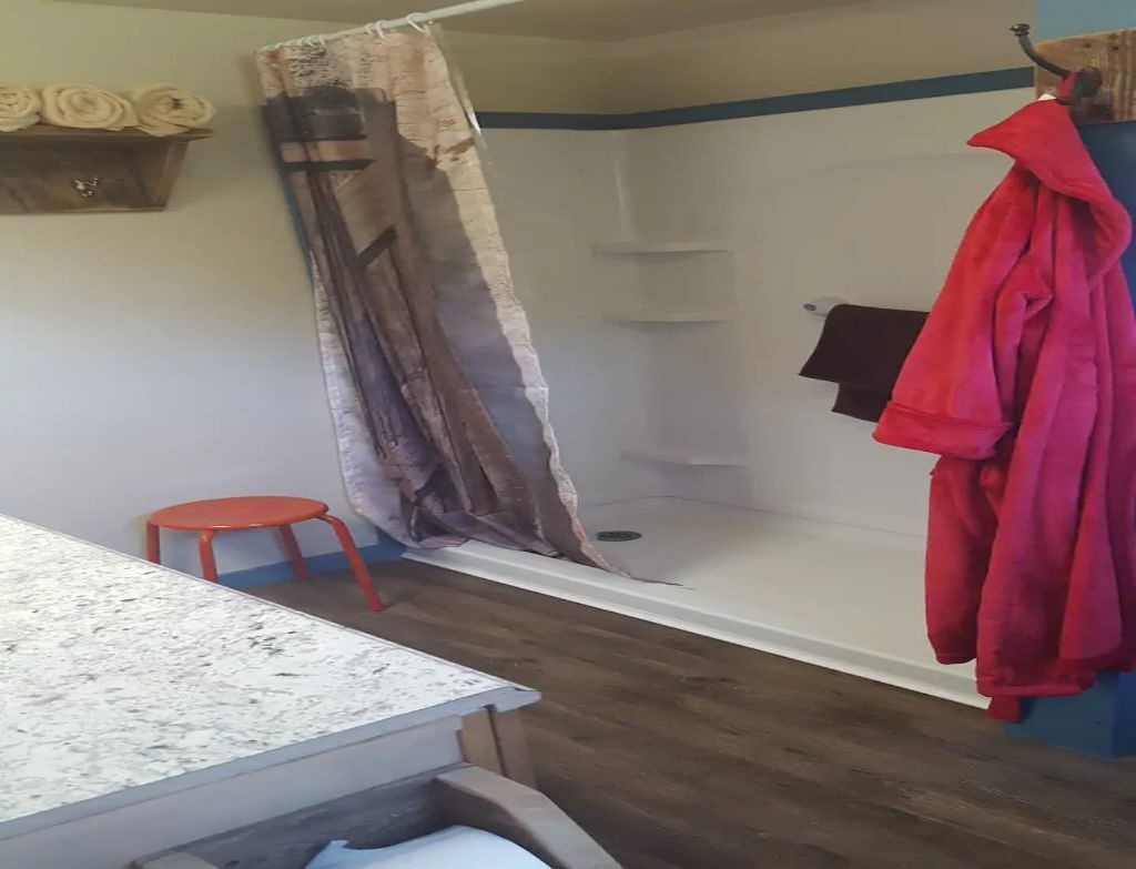 A bathroom with a shower, a red stool, and a red robe hanging on the wall.