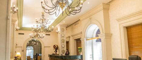 A lobby with a chandelier, reception desk, seating area, and a check-in counter.