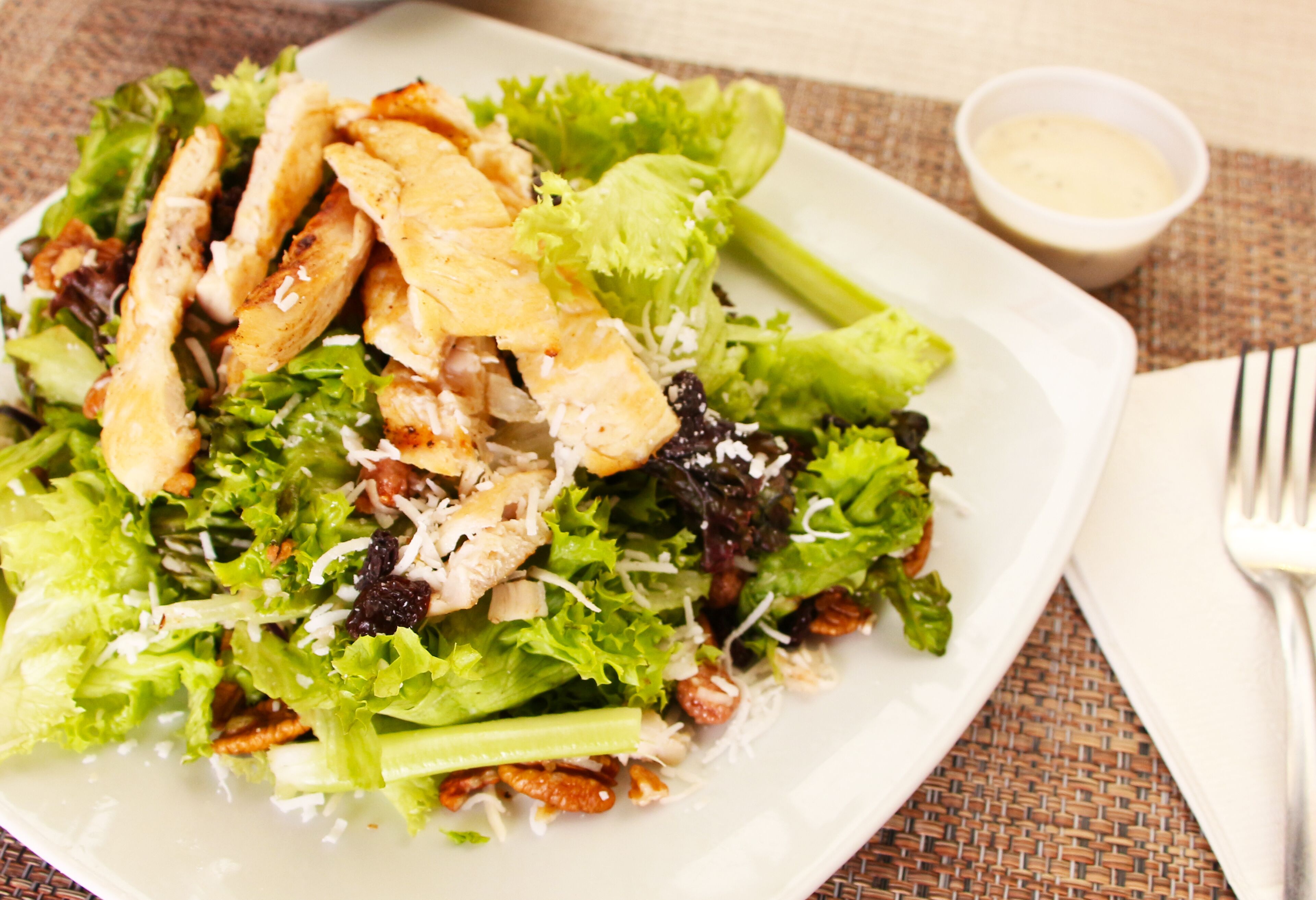 Ein Salat mit Hähnchen, Blattsalat und Nüssen, dazu eine kleine Schüssel mit Dressing.