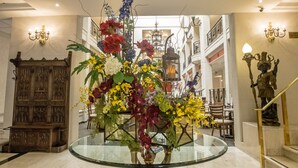 Un vestíbulo con una mesa de vidrio rodeada por un arreglo floral, un techo de vitral y una puerta de madera.