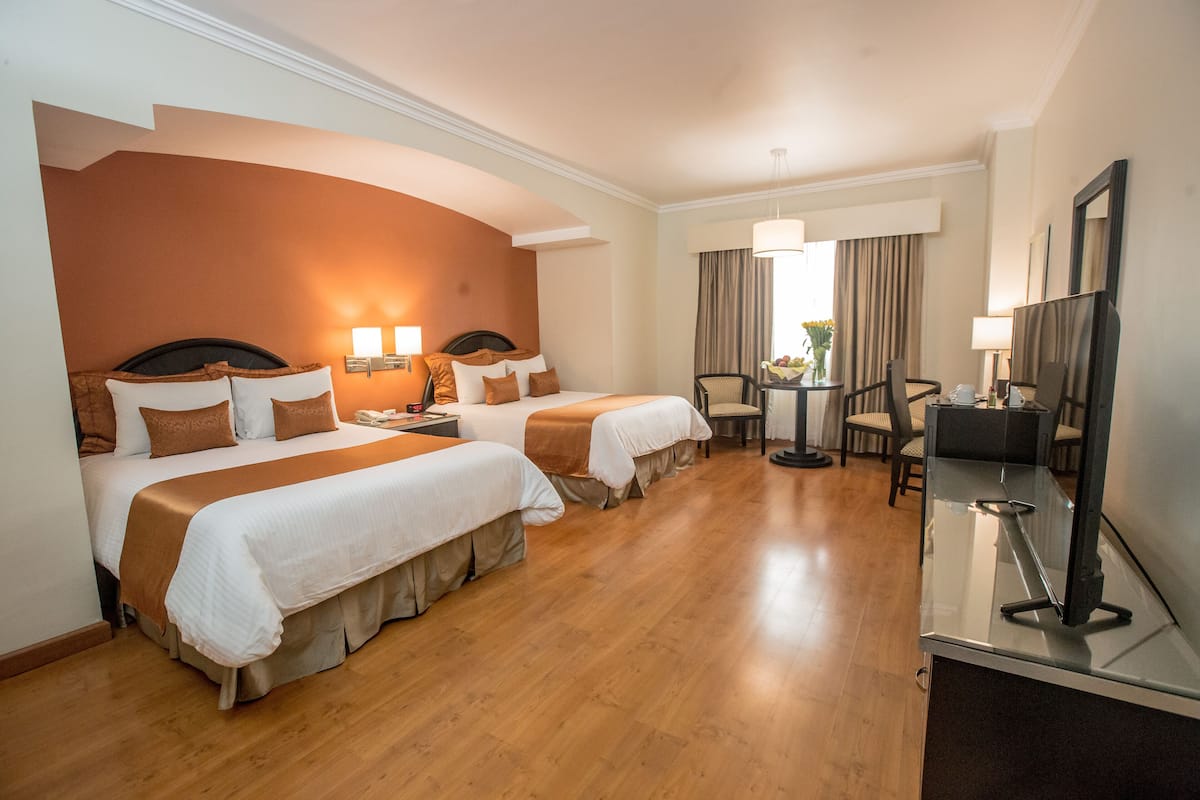 Hotelkamer met twee bedden, een bureau met stoel, een televisie en een kleine tafel met een bloevas.